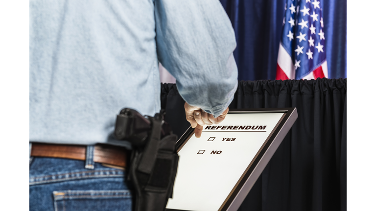 Man with open-carry handgun in holster looking over Referendum ballot