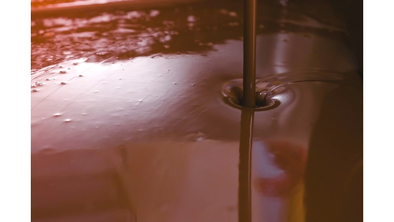 Jet of dark milk chocolate in Chocolate tempering machine. Close-up view.