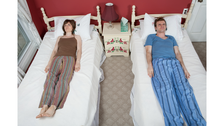 Young couple lying on single beds, ignoring each other