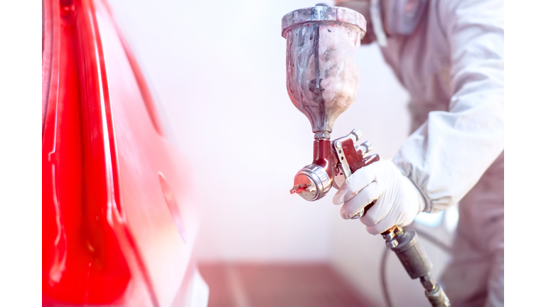 Close-up of spray gun with red paint painting a car
