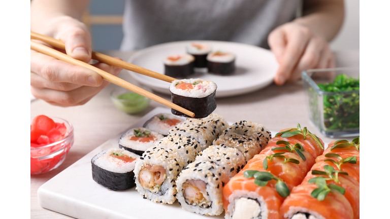 Woman taking tasty sushi roll with salmon from set at table, closeup