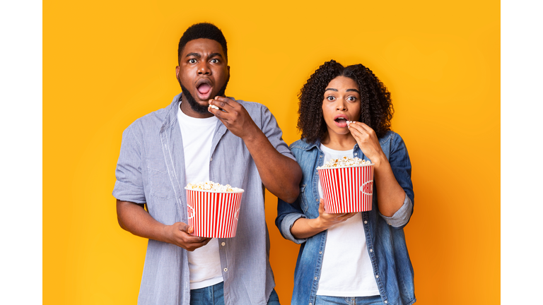 Horror Movie. Shocked african american couple with popcorn buckets over yellow background