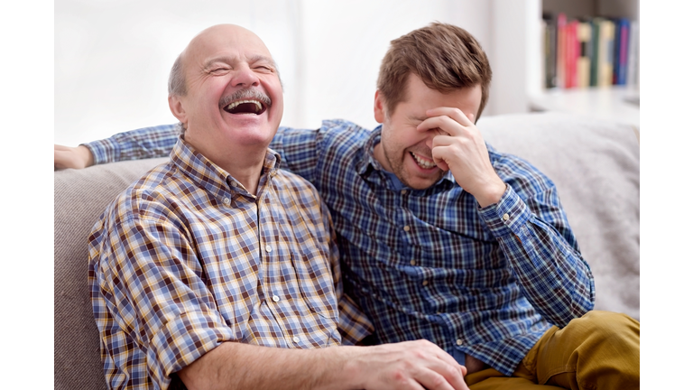 Father and son are sitting on the sofa in the living room and remember joke