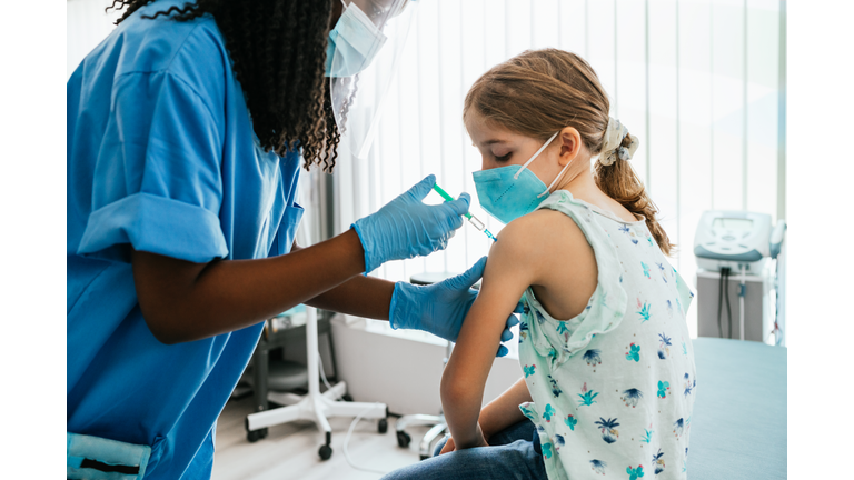 Young girl watching her being injected with COVID-19 vaccine at a medical clinic