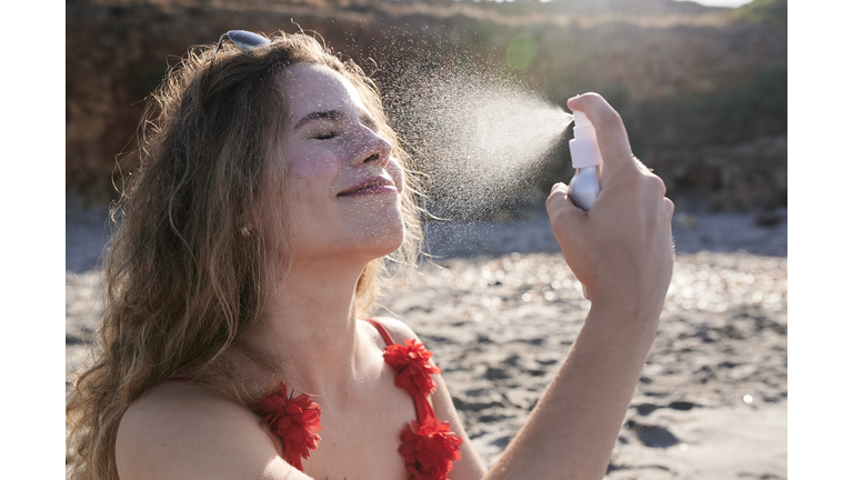 Young woman applying suncream spray on the beach