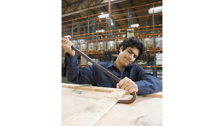 Male warehouse worker opening box with crowbar