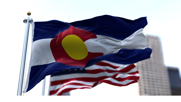 the flag of the US state of Colorado waving in the wind with the American stars and stripes flag blurred in the background