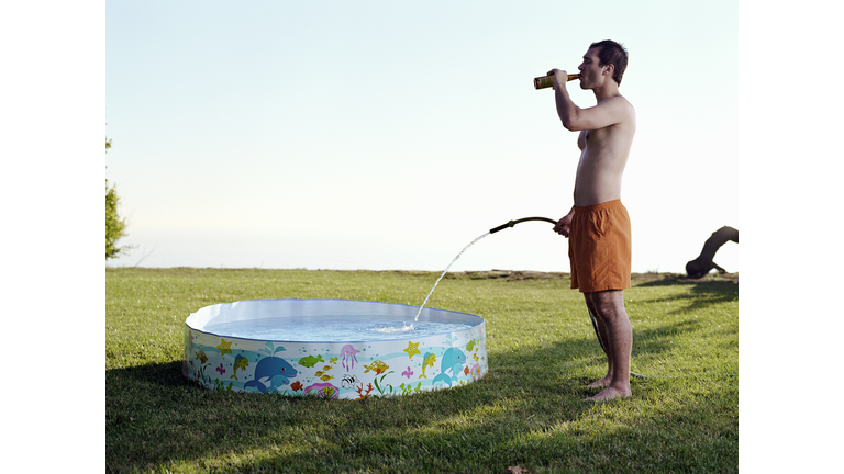 Young man filling plastic pool with water from hose