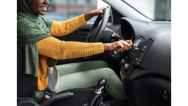 Unrecognizable black muslim woman turning on volume in car audio system