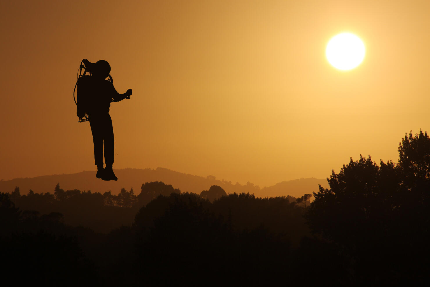 Jetpack Rocket Man flying at Sunset Silhouetted against the Sky