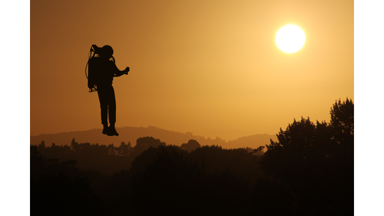 Jetpack Rocket Man flying at Sunset Silhouetted against the Sky