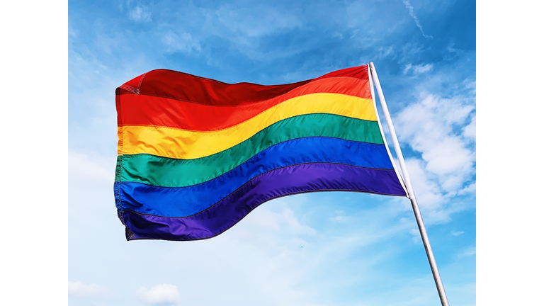 Rainbow flag waving in the wind against blue sky