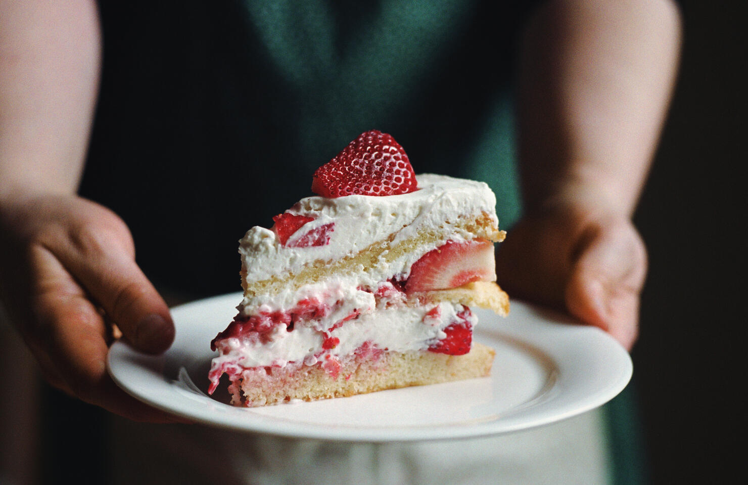 Woman in apron holding slice of strawberry cake