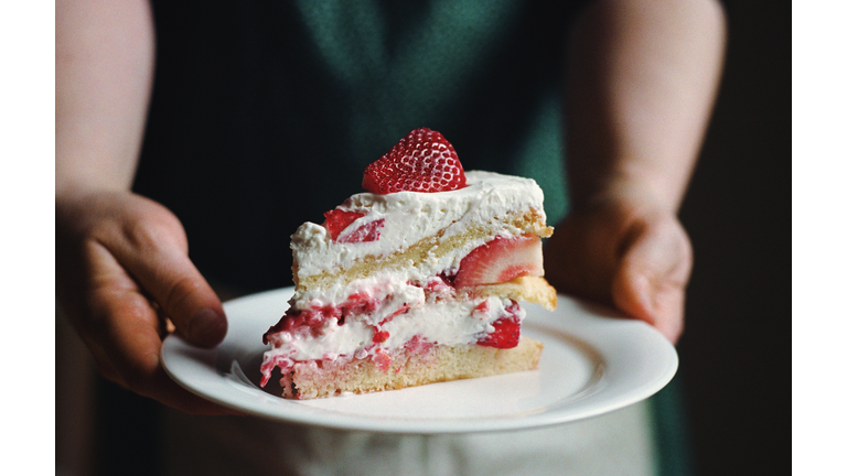 Woman in apron holding slice of strawberry cake