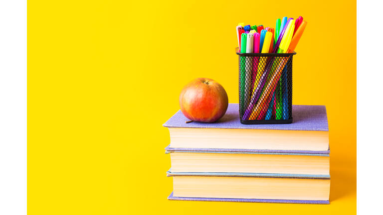 Back to school. Stand with pencils and red apple on the books, on yellow background. The concept of the teachers day, new school year.