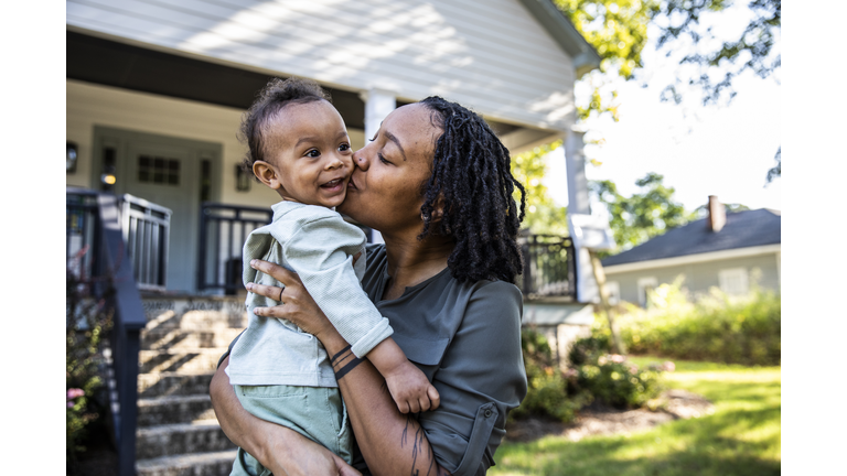Mother holding toddler in front of new home