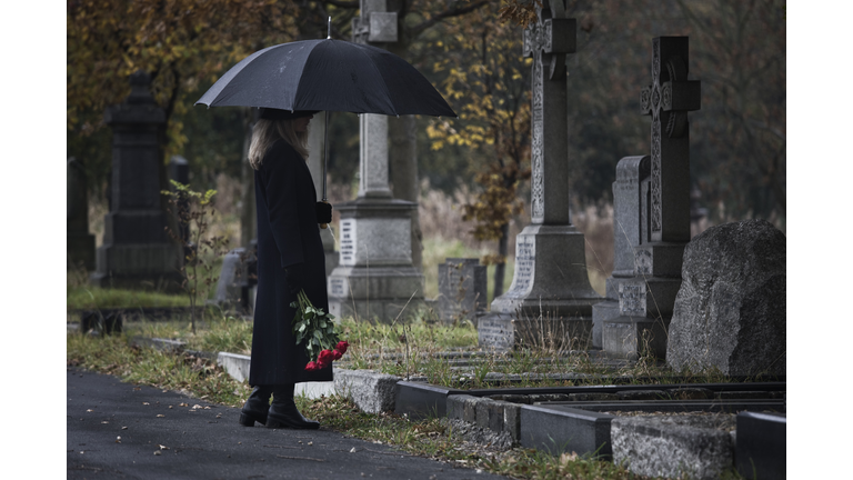 widow bringing roses to a grave in a cemetery