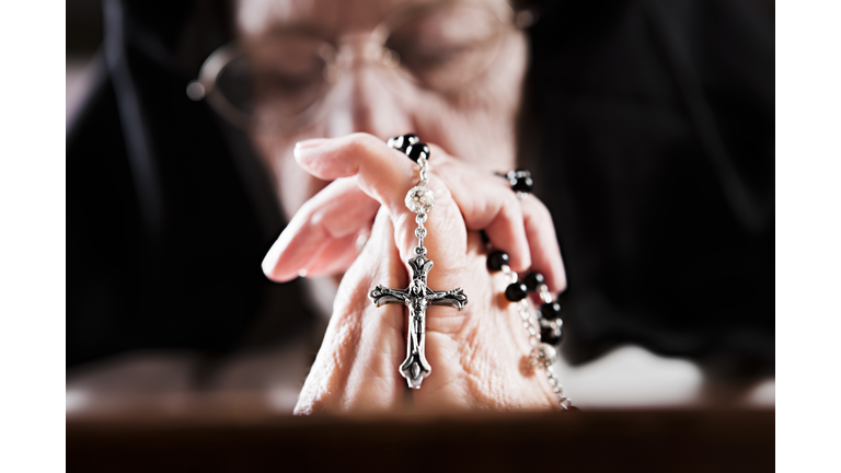 An old nun's hands clasp her rosary as she prays.