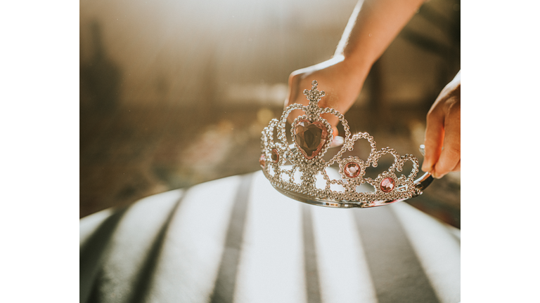 Child picking up a plastic jewelled tiara toy in sunlight