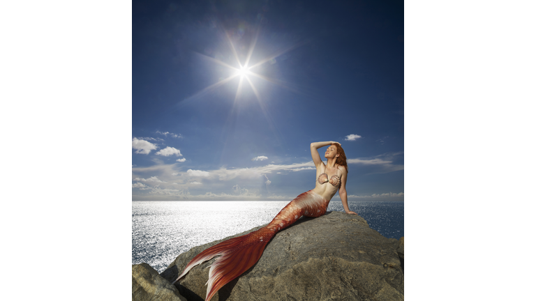 Caucasian mermaid laying on rock near ocean
