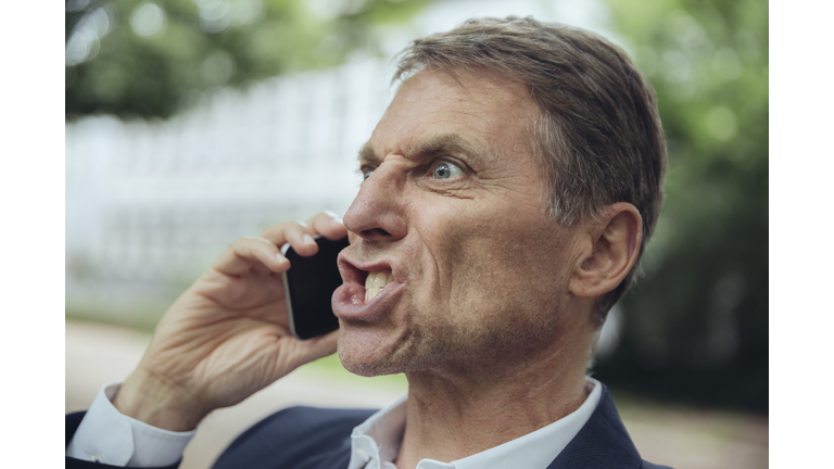 Portrait of angry mature businessman outdoors on the phone