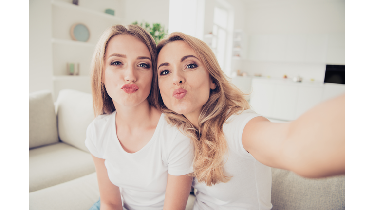 Close up photo of two people pretty mum mommy and teen daughter video call millennials trendy make take selfies duck lips fooling wear white t-shirts jeans sit on comfy sofa couch