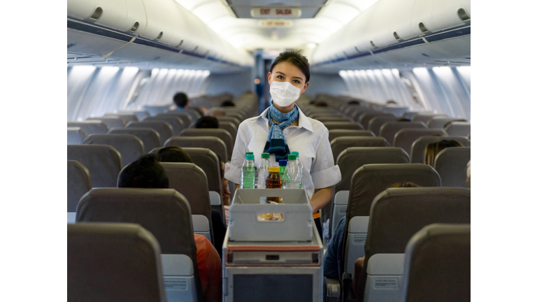 Flight attendant serving drinks in an airplane wearing a facemask