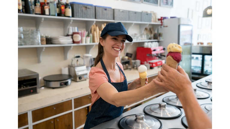 Female worker serving an ice cream to an unrecognizable customer at the ice cream parlor