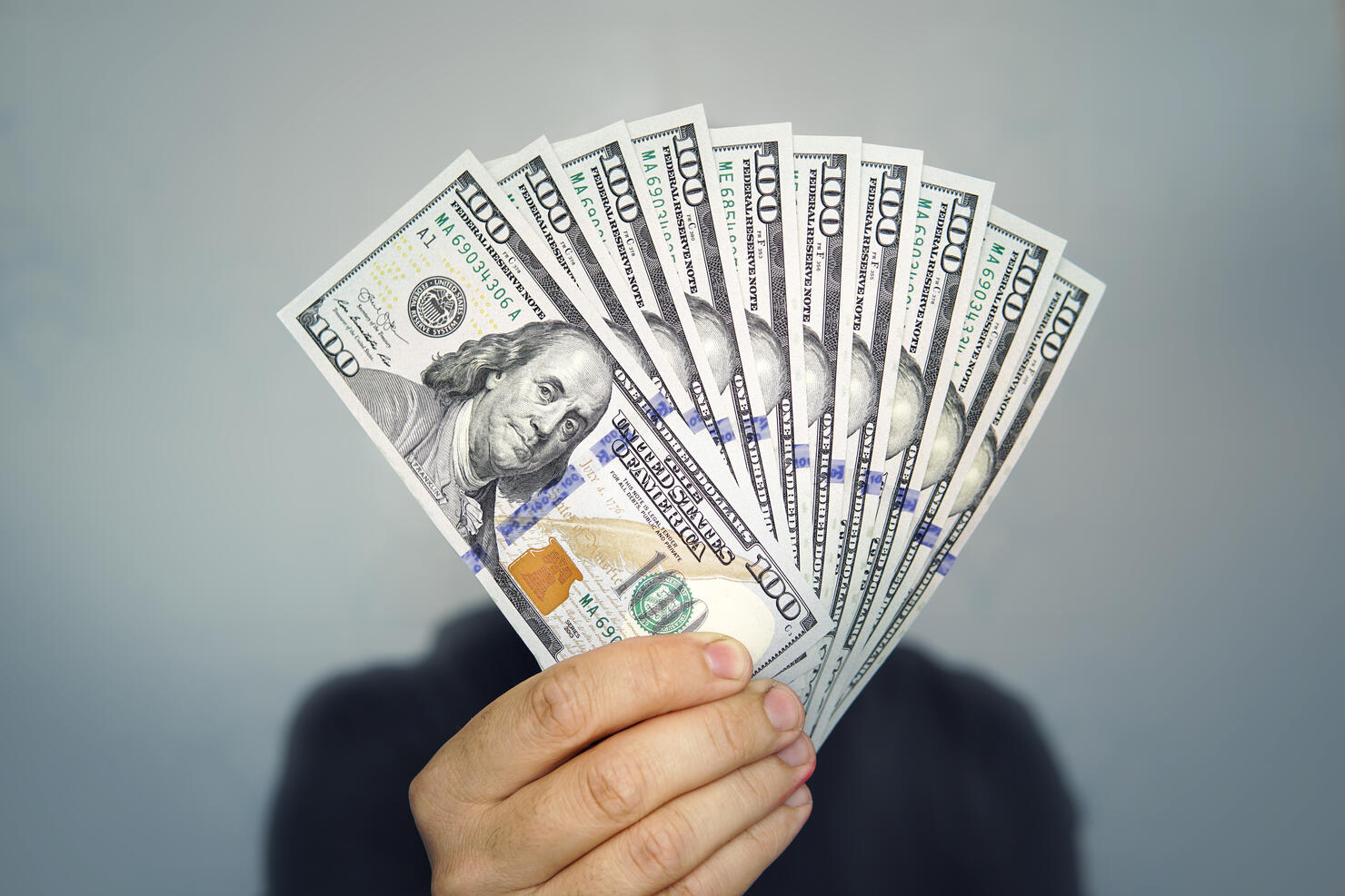 1000 dollars in 100 bills in a man's hand close-up on a dark background. Hands holding dollar cash