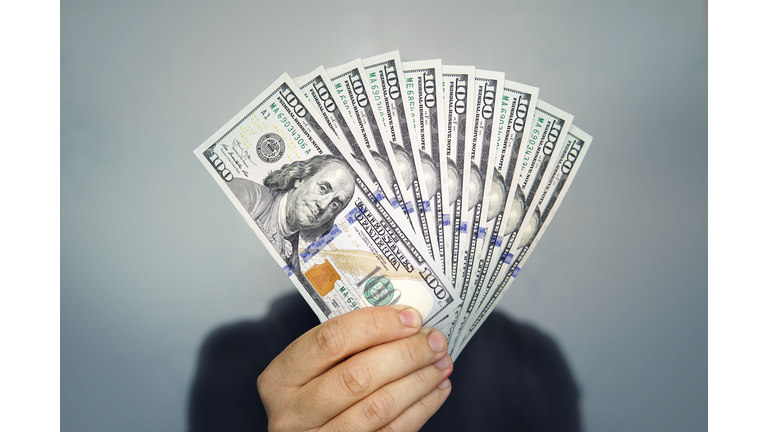 1000 dollars in 100 bills in a man's hand close-up on a dark background. Hands holding dollar cash