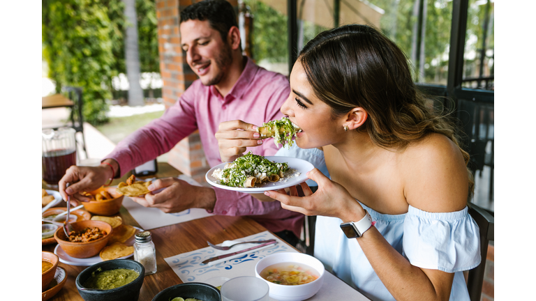 young latin woman eating mexican tacos on a restaurant terrace in Mexico Latin America, feeling happy on a summer day