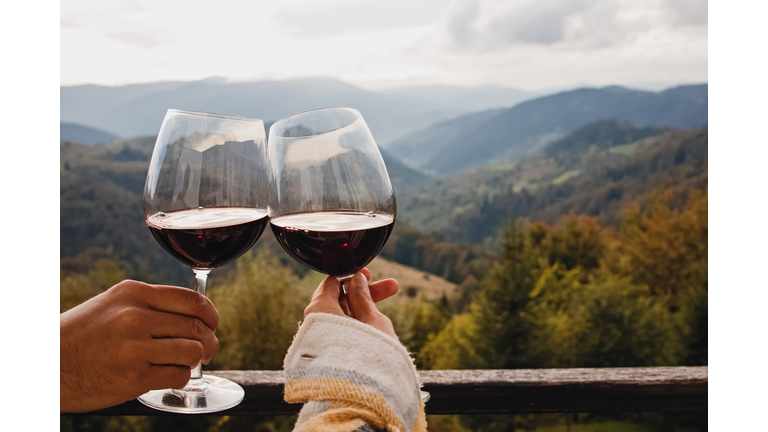 Man and woman clinking with glasses of red wine with a scenic mountain view.