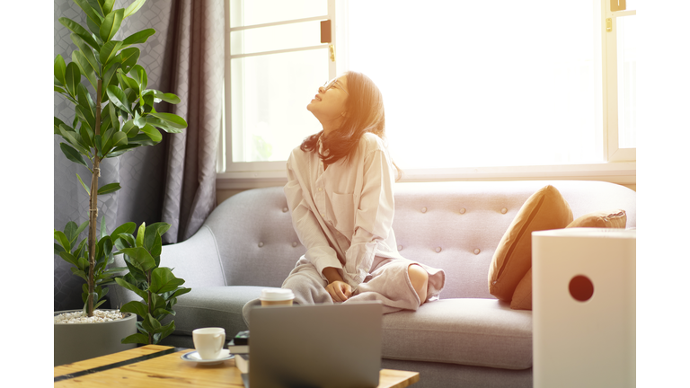 beautiful asian girl female feeling fresh and relax on cozy sofa with air purifier machine