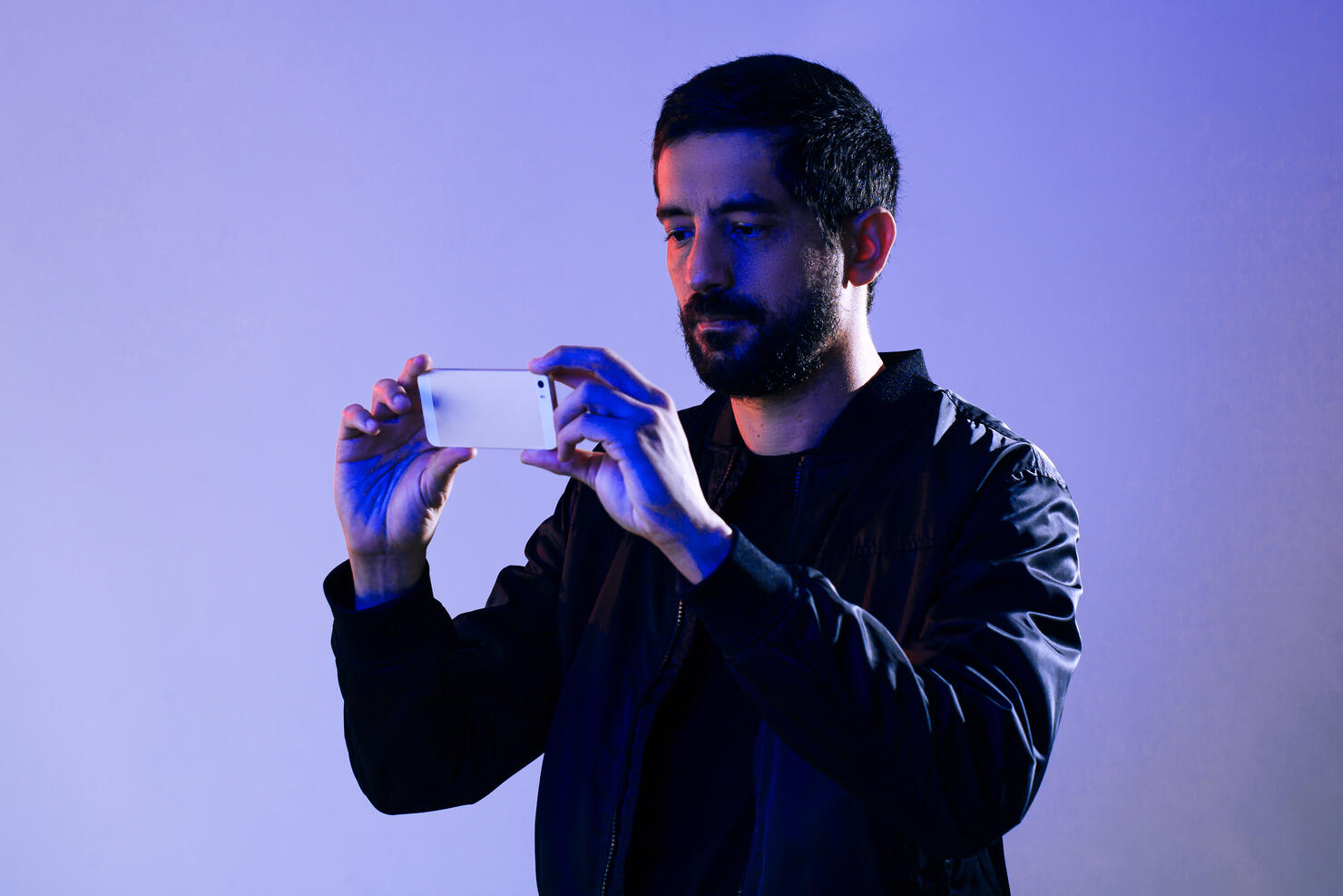 Man wearing jacket and holding cell phone illuminated by blue and red lights. Concept of man filming the police on his smartphone