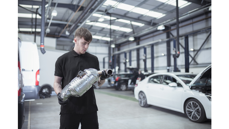 Apprentice holding catalytic converter in car service centre