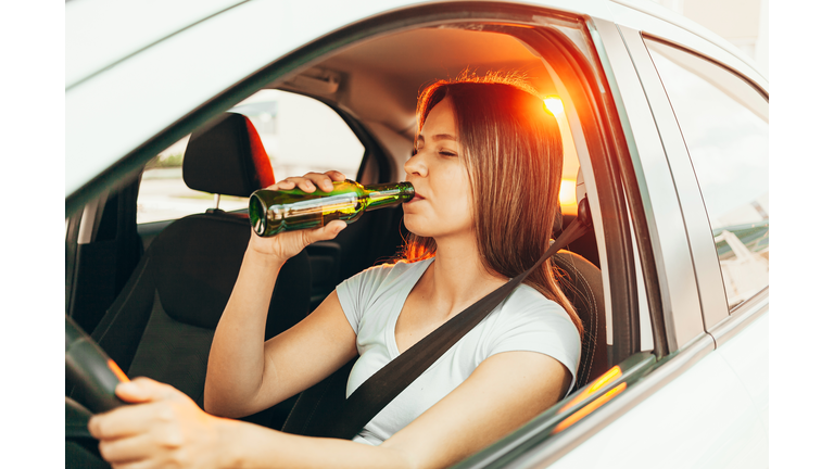 Drunk young woman drives a car with a bottle of beer