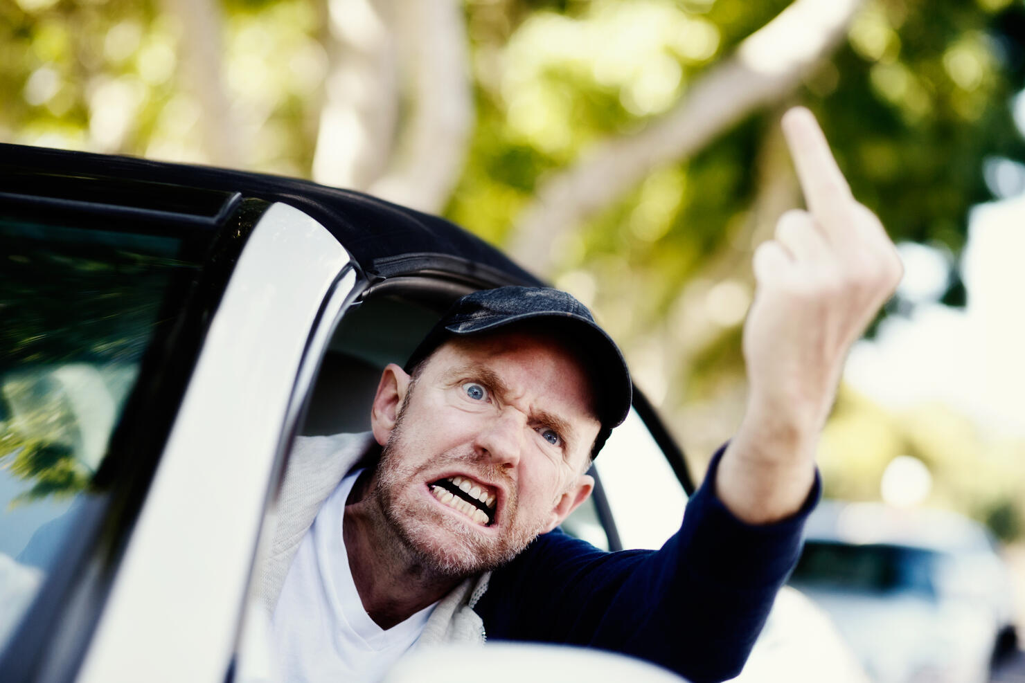 Grimacing male driver makes obscene gesture at someone