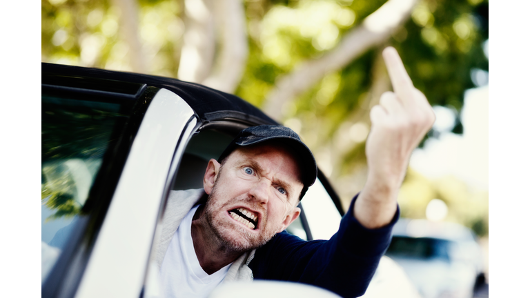 Grimacing male driver makes obscene gesture at someone