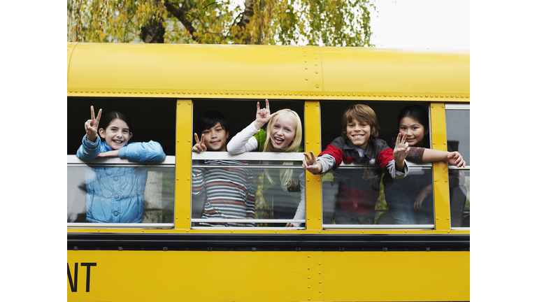 Group of young students hanging out bus windows