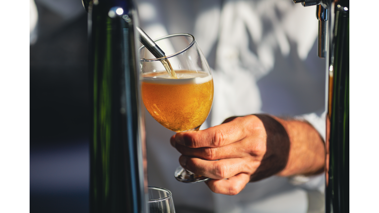 Shallow depth of field (selective focus) image with a man pouring craft beer from a dispenser into a glass.