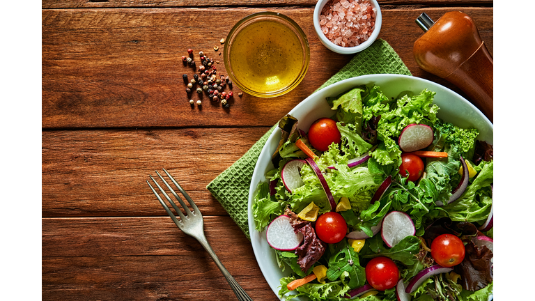Top view of fresh and healthy salad in a bowl on wooden table.