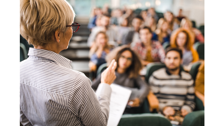 Rear view of mature teacher giving a lecture in a classroom.