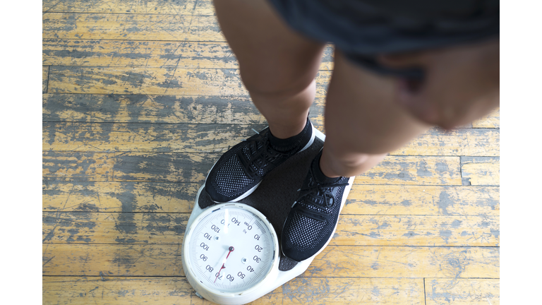 Low section of man checking weight on scale in gym