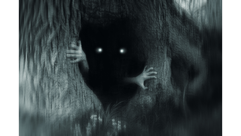 A spooky horror concept of a monster with glowing eyes, hiding in a tree trunk, in a dark spooky forest. With a grunge, blurred, edit.