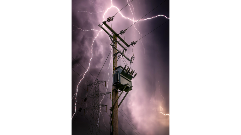 Bright lightning bolts striking electric power pylon tower cables and sub station strike. Electricity discharge cloud to ground storm with transformer on wooden telegraph pole silhouette against sky.