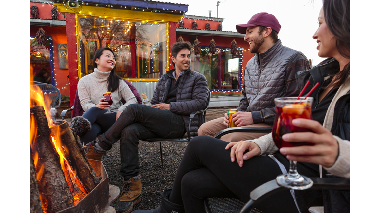 Couples drinking cocktails and beer outdoors at storefront campfire