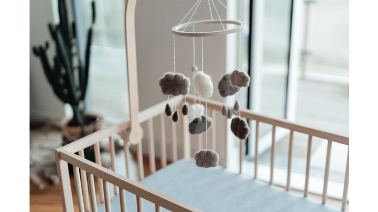 Stylish Scandinavian newborn baby nursery with natural wooden baby cot and handmade mobile hanging over it