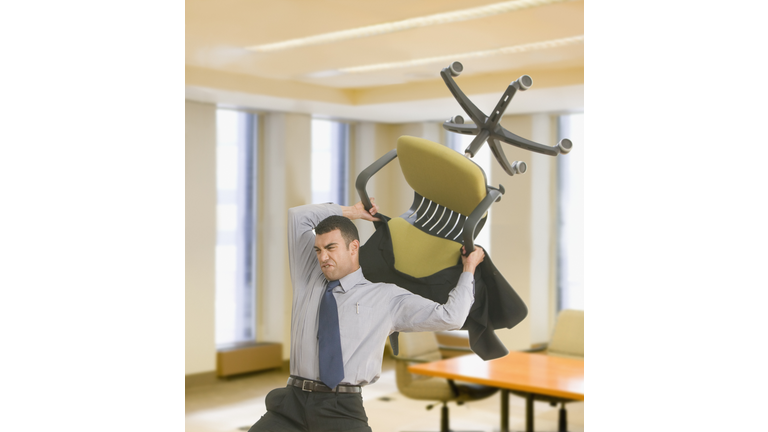 Hispanic businessman throwing chair