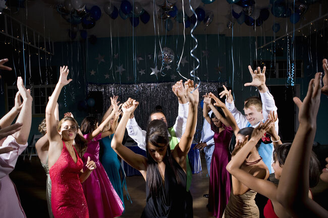 Teenagers (15-18) in formalwear dancing at prom, arms raised