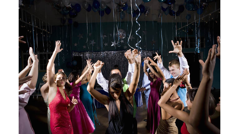 Teenagers (15-18) in formalwear dancing at prom, arms raised